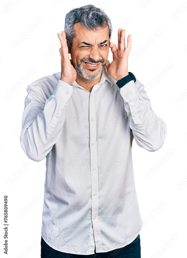 Middle age hispanic with grey hair wearing casual white shirt covering ears with fingers with annoyed expression for the noise of loud music. deaf concept. Middle age hispanic with grey hair wearing casual white shirt covering ears with fingers with annoyed expression for the noise of loud music. deaf concept.