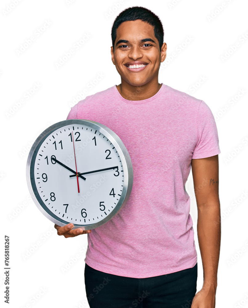 Young handsome hispanic man holding big clock looking positive and happy standing and smiling with a confident smile showing teeth Young handsome hispanic man holding big clock looking positive and happy standing and smiling with a confident smile showing teeth