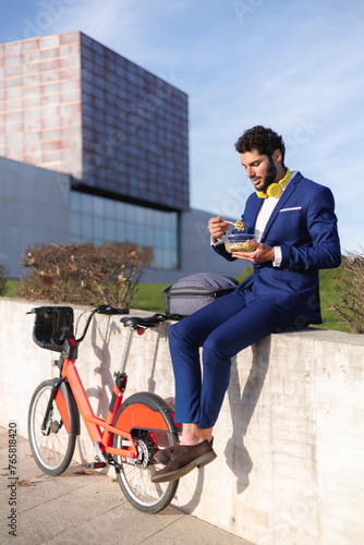 Healthy company culture. Male employee with a healthy lifestyle eating a salad with next to a bike.