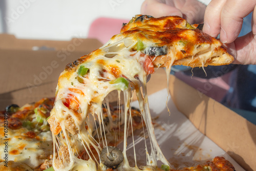 Hand holding slice of hot pizza