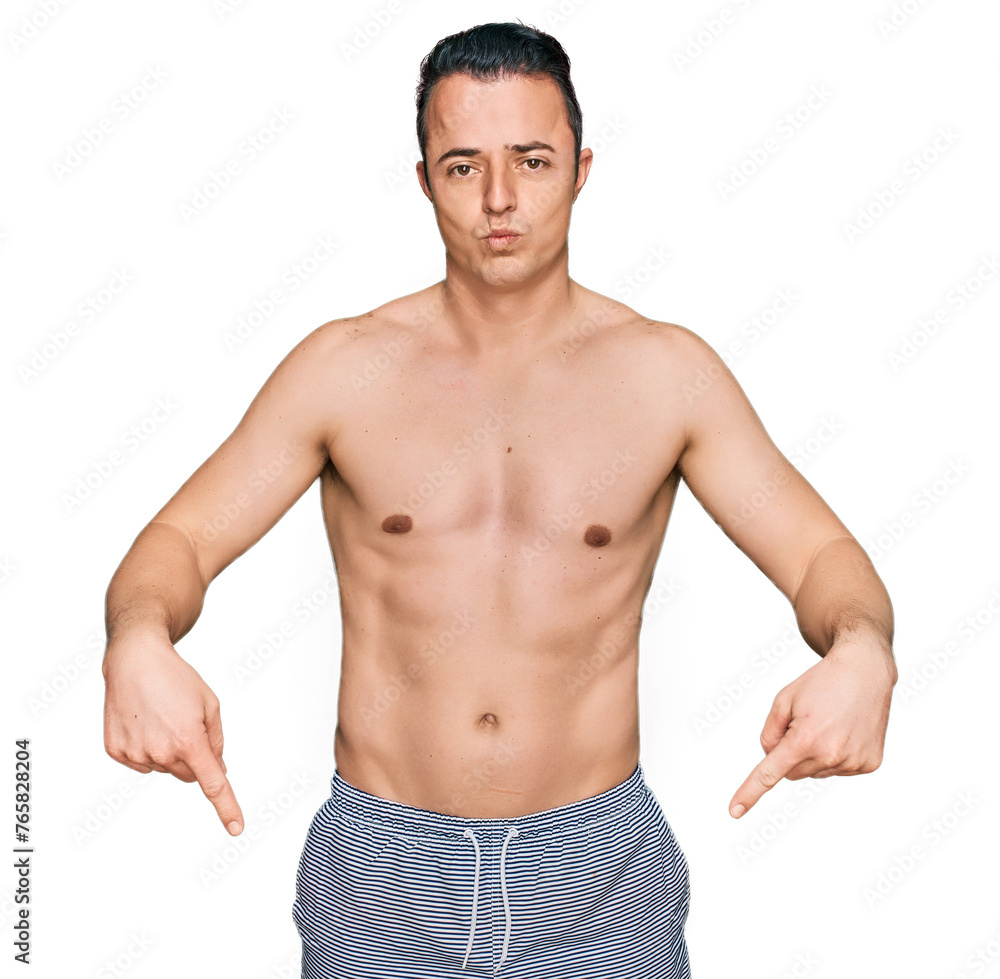 Handsome young man wearing swimwear shirtless pointing down looking sad and upset, indicating direction with fingers, unhappy and depressed. Handsome young man wearing swimwear shirtless pointing down looking sad and upset, indicating direction with fingers, unhappy and depressed.