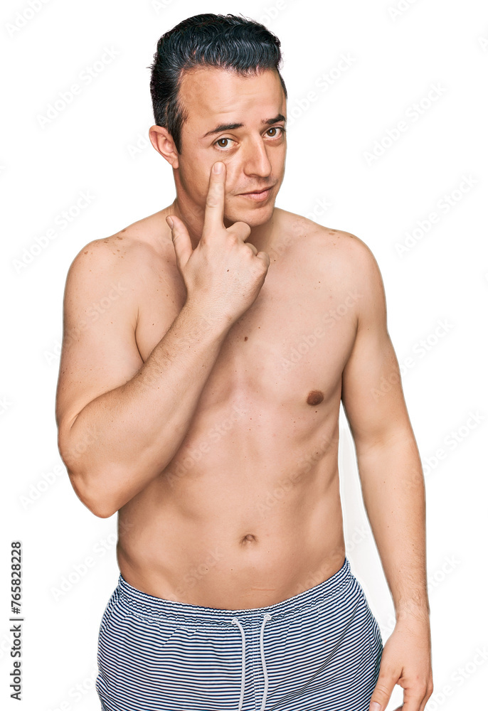 Handsome young man wearing swimwear shirtless pointing to the eye watching you gesture, suspicious expression Handsome young man wearing swimwear shirtless pointing to the eye watching you gesture, suspicious expression