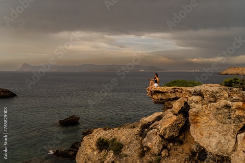Contemplando el Horizonte na mujer se encuentra sentada en un acantilado, contemplando el mar y respirando el aire fresco. La majestuosidad del paisaje y la tranquilidad del momento