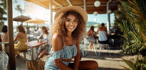 young adult woman at a beach bar or beach cafe, joyful smile, happy relaxed. Straw hat sun hat on vacation or summer outside in the sunshine