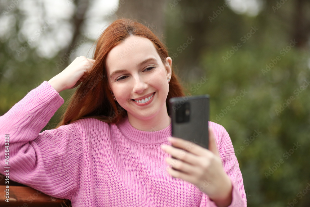 Pretty teenage girl takes a selfie with her cell phone while walking in the park