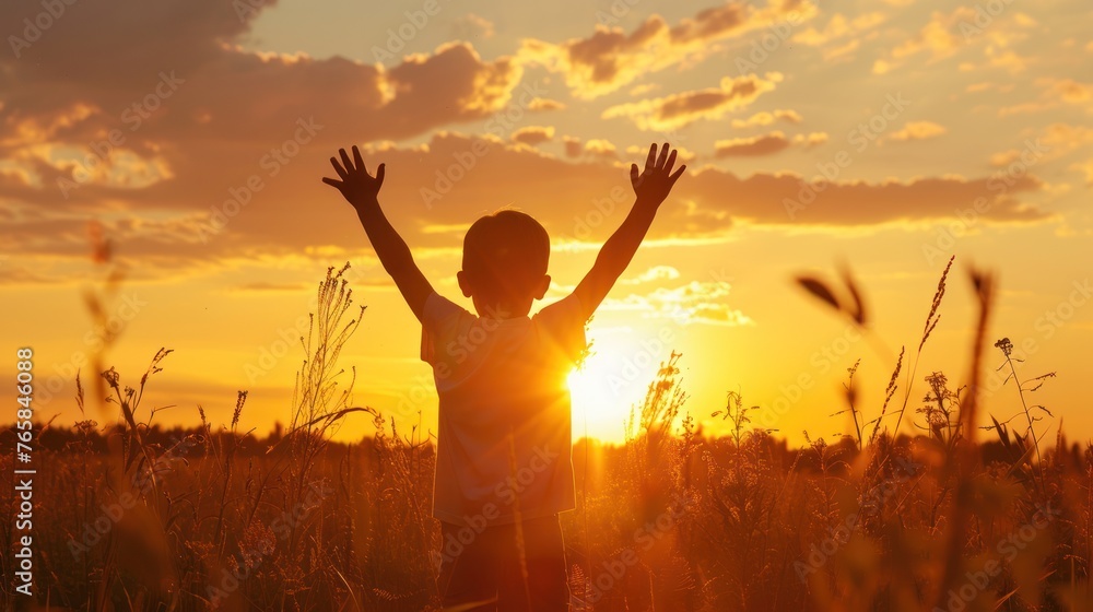 little boy raises his hands above the sunset sky