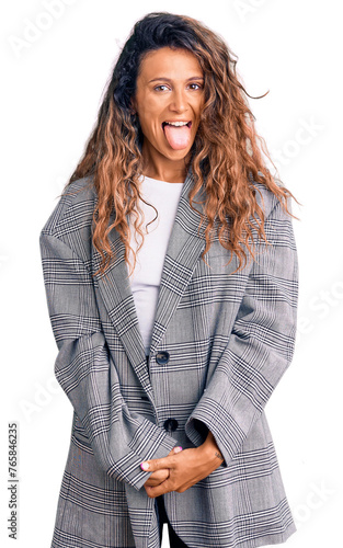 Young hispanic woman with tattoo wearing business oversize jacket sticking tongue out happy with funny expression. emotion concept.