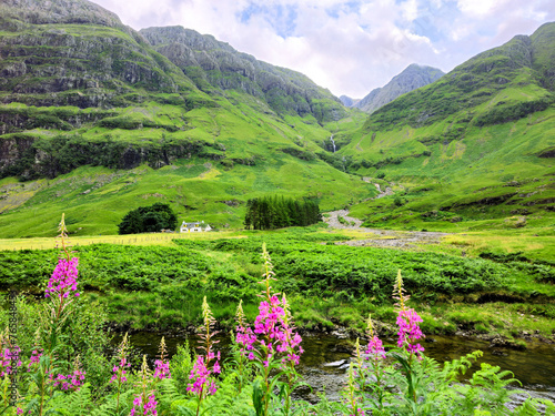 Beautiful lush Scottish Highlands of Glen Coe with flowers, waterfall and traditional house, Scotland, UK.