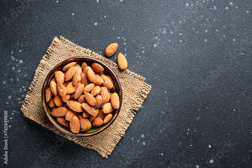 Almond nuts in bowl at black background. Top view.
