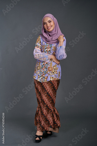 Beautiful female model wearing modern batik kebaya, sitting on a chair isolated over grey background. Eidul fitri festival fashion and beauty concept.	 photo