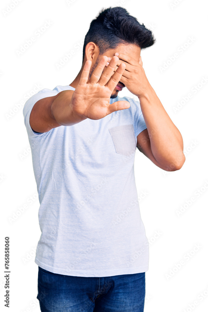 Handsome latin american young man wearing casual clothes covering eyes with hands and doing stop gesture with sad and fear expression. embarrassed and negative concept. Handsome latin american young man wearing casual clothes covering eyes with hands and doing stop gesture with sad and fear expression. embarrassed and negative concept.
