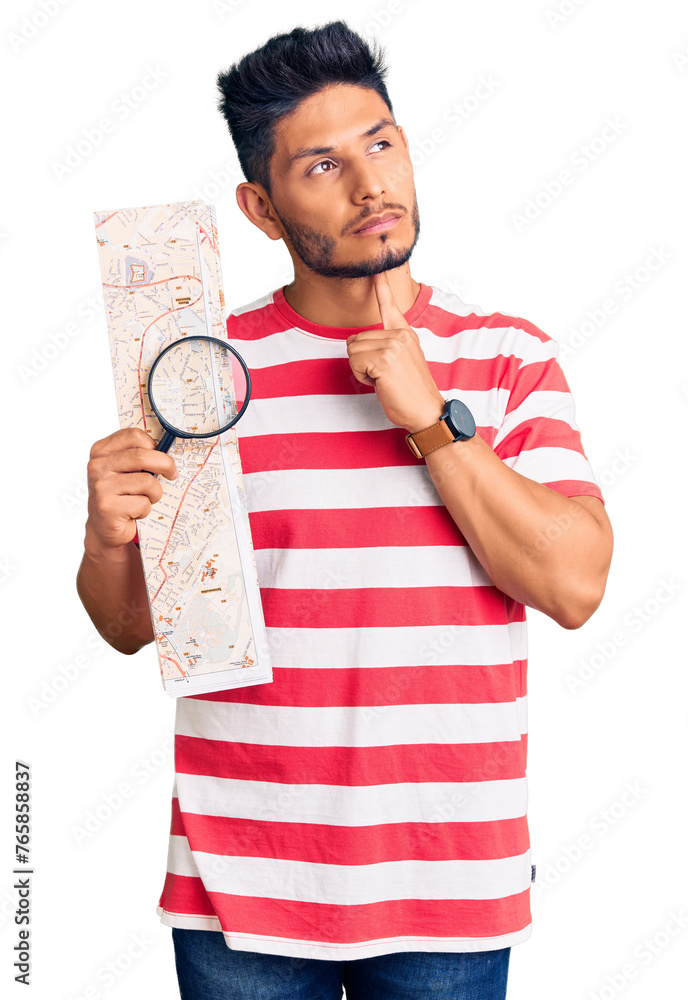 Handsome latin american young man looking at city map with magnifying glass serious face thinking about question with hand on chin, thoughtful about confusing idea Handsome latin american young man looking at city map with magnifying glass serious face thinking about question with hand on chin, thoughtful about confusing idea