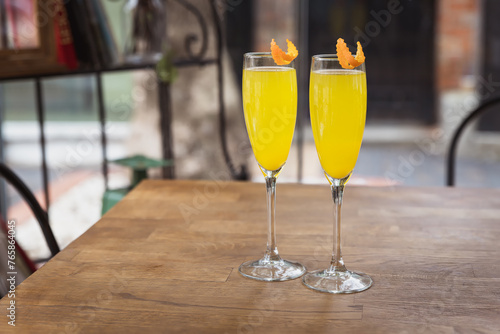 Orange girly champagne cocktails on wooden restaurant table outdoors, mimosa drink in two flutes
