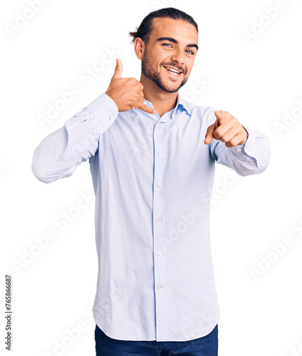 Young handsome man wearing business clothes smiling doing talking on the telephone gesture and pointing to you. call me.