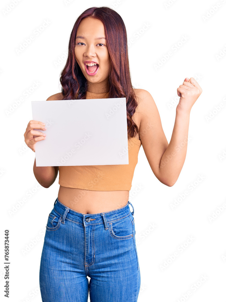 Young beautiful chinese girl holding paper banner with blank space screaming proud, celebrating victory and success very excited with raised arms Young beautiful chinese girl holding paper banner with blank space screaming proud, celebrating victory and success very excited with raised arms