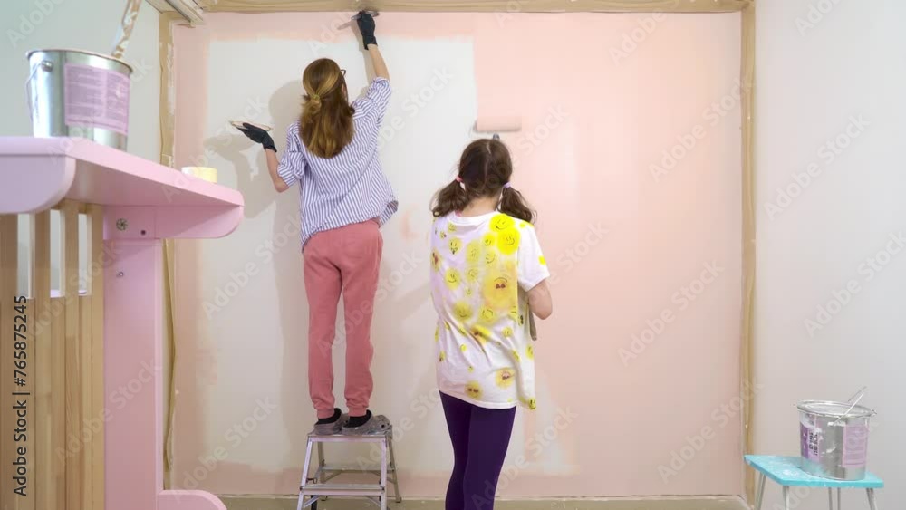 Back view of happy mother and daughter painting house wall in pink color using roller brush in apartment renovating home. House redesigning, renovating and repair concept. Back view of happy mother and daughter painting house wall in pink color using roller brush in apartment renovating home. House redesigning, renovating and repair concept.