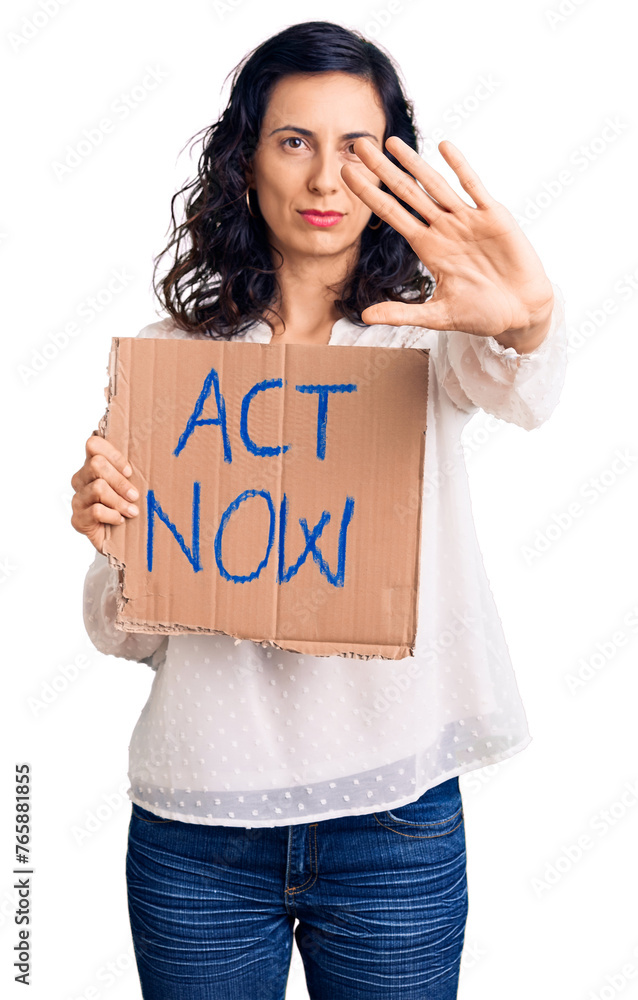 Young beautiful hispanic woman holding act now banner with open hand doing stop sign with serious and confident expression, defense gesture Young beautiful hispanic woman holding act now banner with open hand doing stop sign with serious and confident expression, defense gesture