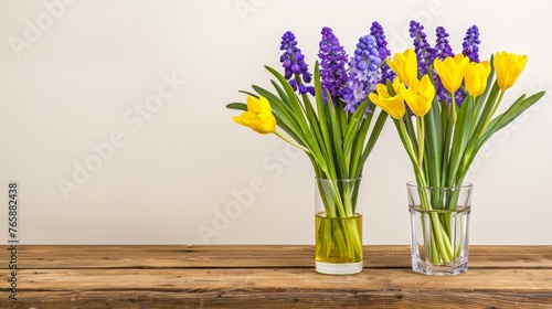  two vases filled with yellow and purple flowers on top of a wooden table in front of a white wall. © Anna