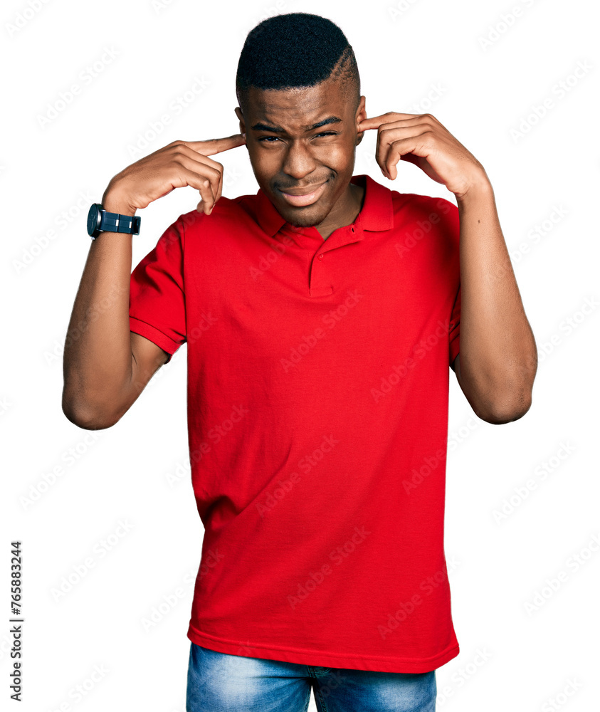 Young african american man wearing casual red t shirt covering ears with fingers with annoyed expression for the noise of loud music. deaf concept. Young african american man wearing casual red t shirt covering ears with fingers with annoyed expression for the noise of loud music. deaf concept.