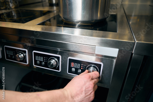 Cropped chef turning on button of electric stove for heating dish in saucepan
