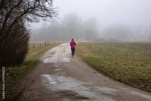 Natural landscape of a foggy morning in the countryside and an athletic woman runs along the road in sportswear.