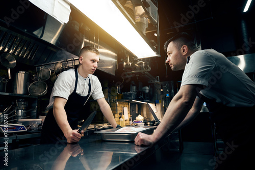 Fotografie Competitor chefs with knives looking at each other at table in restaurant