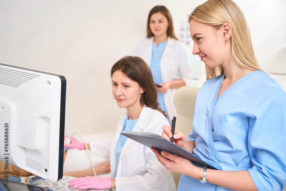 Fototapeta premium Gynecologist doing ultrasound scan of woman belly and doctor writing examining