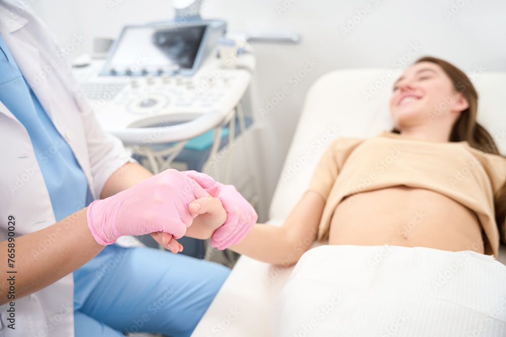 Partial gynecologist and blurred young woman holding hands in ultrasound room Partial gynecologist and blurred young woman holding hands in ultrasound room