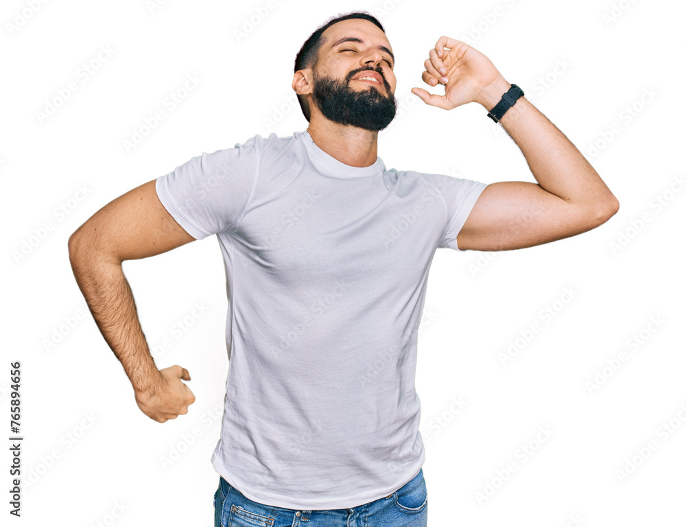 Young man with beard wearing casual white t shirt stretching back, tired and relaxed, sleepy and yawning for early morning Young man with beard wearing casual white t shirt stretching back, tired and relaxed, sleepy and yawning for early morning
