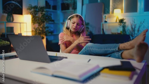 Carefree young girl in headphones listening to music instead of doing homework photo