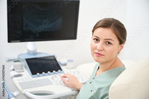 Female doctor looking at camera while working on ultrasound machine in clinic