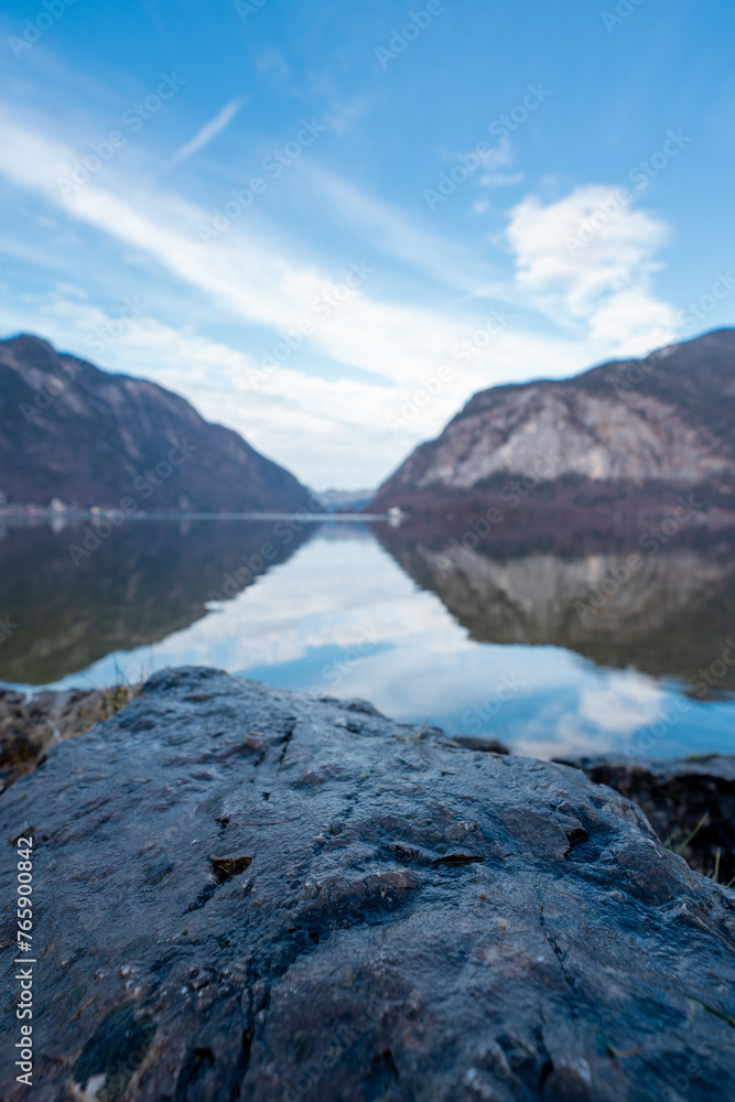 Capture the serenity of nature with this breathtaking photo: a solitary stone rests upon a cliff overlooking a pristine alpine lake, framed by majestic mountains