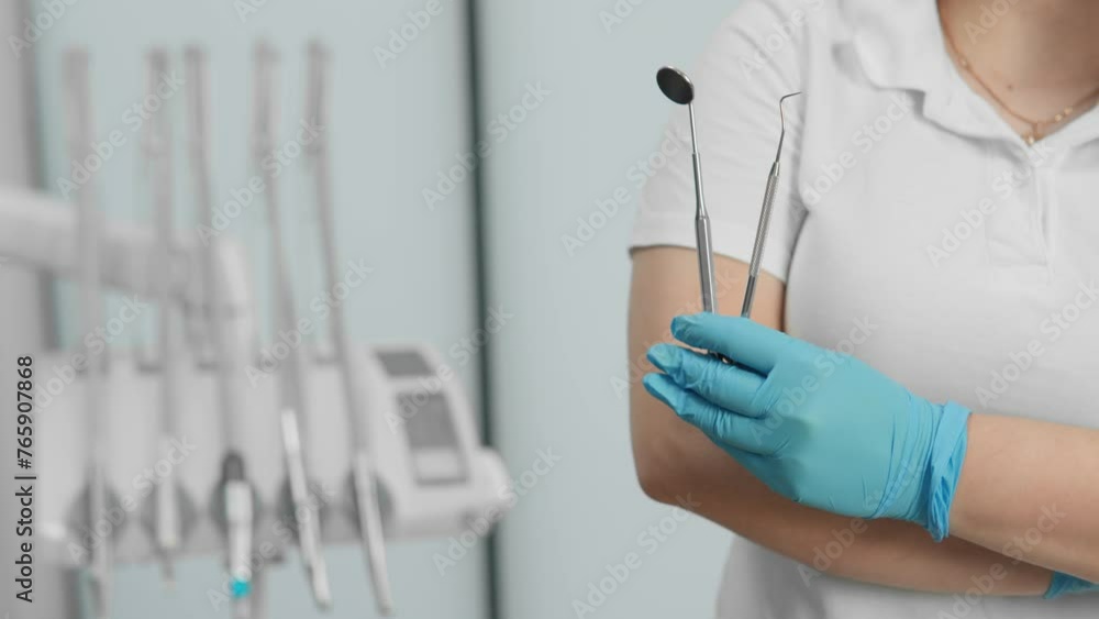 A dentist holds his instruments in his hand. In the background is a dental chair in a dental clinic. A dentist holds his instruments in his hand. In the background is a dental chair in a dental clinic.