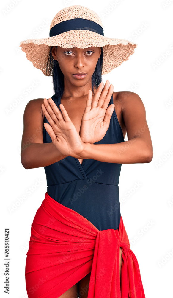 Young african american woman wearing swimsuit and summer hat rejection expression crossing arms doing negative sign, angry face Young african american woman wearing swimsuit and summer hat rejection expression crossing arms doing negative sign, angry face
