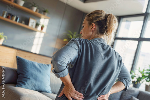 A woman with a backache in a living room. pain. Hand of woman holding her waist backache in pain. Health care concept