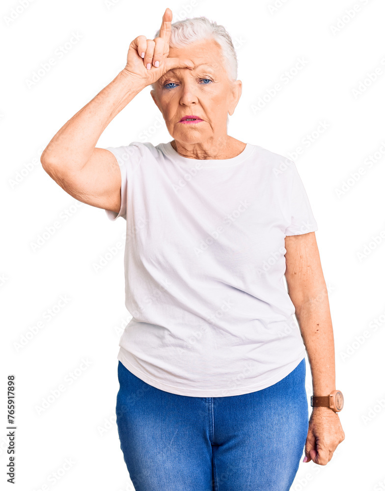 Senior beautiful woman with blue eyes and grey hair wearing casual white tshirt making fun of people with fingers on forehead doing loser gesture mocking and insulting. Senior beautiful woman with blue eyes and grey hair wearing casual white tshirt making fun of people with fingers on forehead doing loser gesture mocking and insulting.