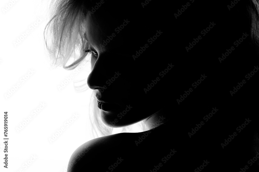 Beautiful sexy woman with big wavy hair and classic make-up studio portrait in bright background. Model silhouette partly illuminated with light. Girl looking away. Black and white image