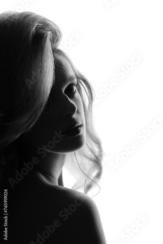 Beautiful sexy woman with big wavy hair and classic make-up studio portrait in bright background. Model silhouette partly illuminated with light. Girl looking at camera. Black and white image © Rytis