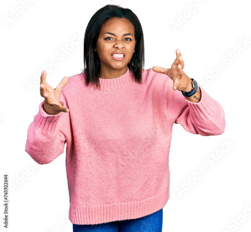 Beautiful hispanic woman wearing casual winter sweater shouting frustrated with rage, hands trying to strangle, yelling mad