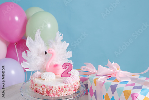White and pink cake decorated with a flamingo figure, white feather wings and number two candle
