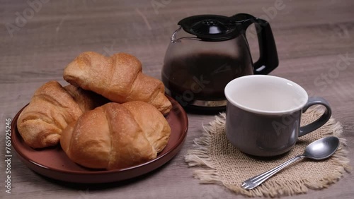 Cornetti nel piatto per la colazione con caffè nella tazza, caraffa con caffè sulla tavola photo