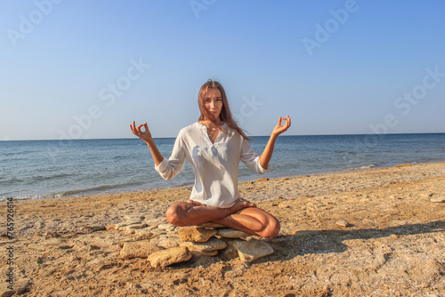 A beautiful girl sits on a stone in the lotus position against the background of the sea and sky