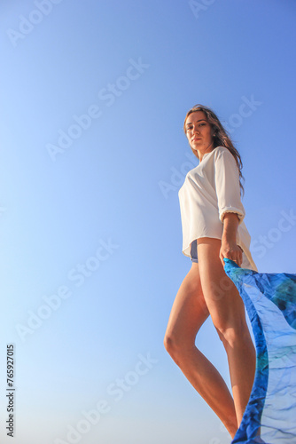 Beautiful girl against the background of a clear sky with a blue pareo in her hands