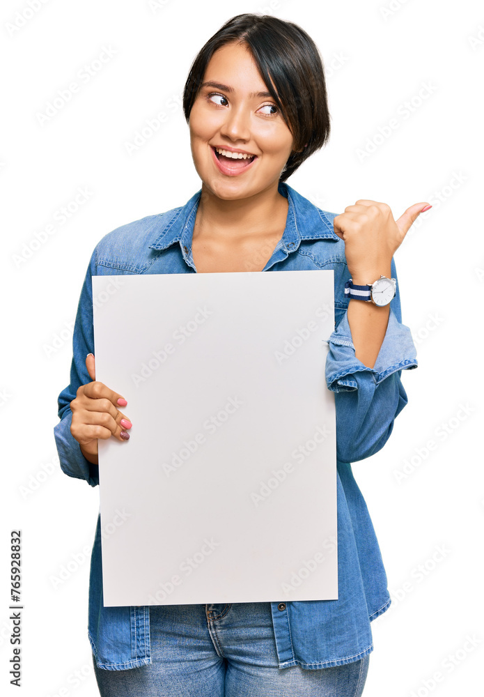 Beautiful young woman with short hair holding blank empty banner pointing thumb up to the side smiling happy with open mouth Beautiful young woman with short hair holding blank empty banner pointing thumb up to the side smiling happy with open mouth
