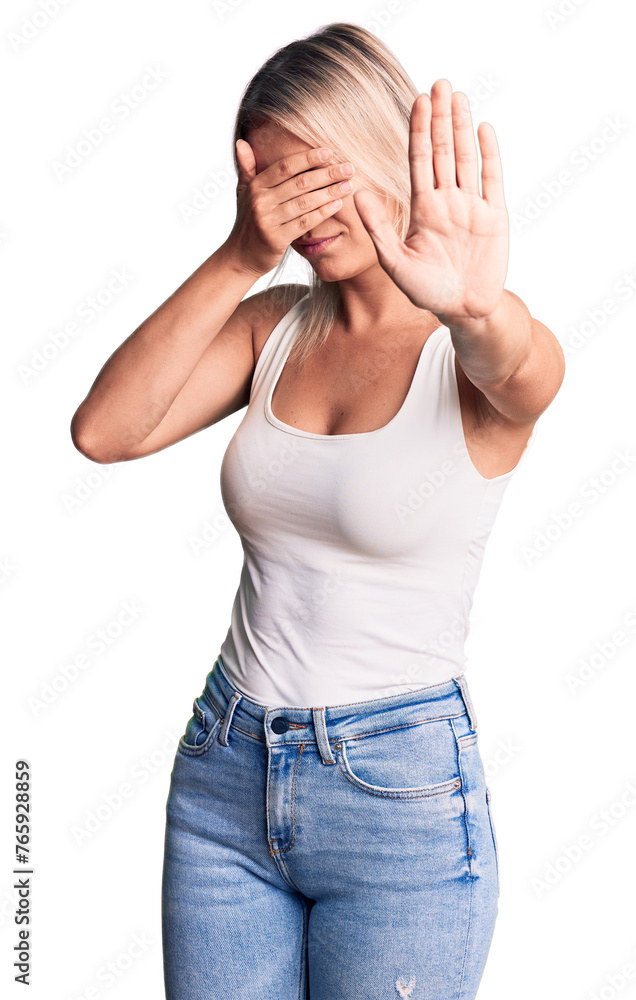 Young beautiful blonde woman wearing casual sleeveless t-shirt covering eyes with hands and doing stop gesture with sad and fear expression. embarrassed and negative concept. Young beautiful blonde woman wearing casual sleeveless t-shirt covering eyes with hands and doing stop gesture with sad and fear expression. embarrassed and negative concept.