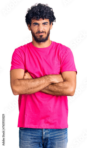 Handsome young man with curly hair and bear wearing casual pink tshirt skeptic and nervous, disapproving expression on face with crossed arms. negative person.