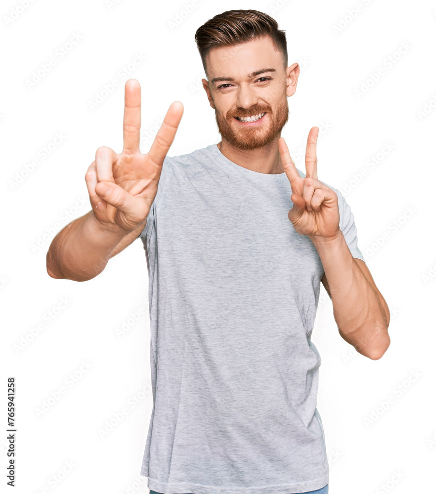 Young redhead man wearing casual grey t shirt smiling looking to the camera showing fingers doing victory sign. number two. Young redhead man wearing casual grey t shirt smiling looking to the camera showing fingers doing victory sign. number two.