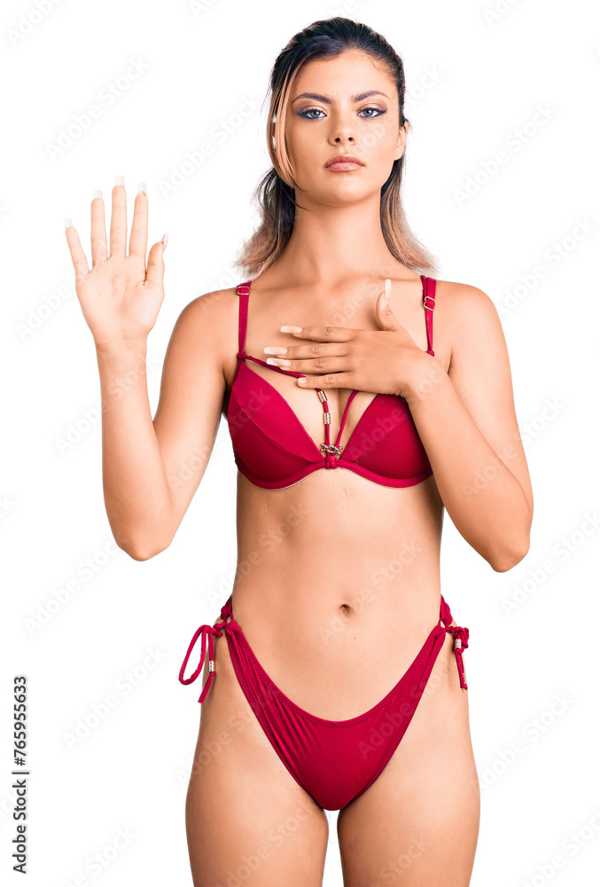 Young beautiful woman wearing bikini swearing with hand on chest and open palm, making a loyalty promise oath Young beautiful woman wearing bikini swearing with hand on chest and open palm, making a loyalty promise oath