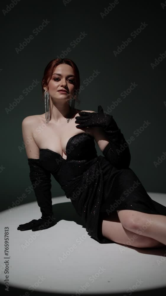 Woman in evening dress poses sitting on floor in studio under spotlight. Concept Spotlight Contemplation Woman in evening dress poses sitting on floor in studio under spotlight. Concept Spotlight Contemplation