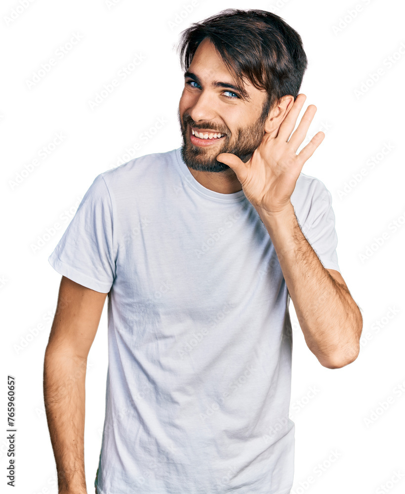 Hispanic man with blue eyes wearing casual white t shirt smiling with hand over ear listening and hearing to rumor or gossip. deafness concept. Hispanic man with blue eyes wearing casual white t shirt smiling with hand over ear listening and hearing to rumor or gossip. deafness concept.